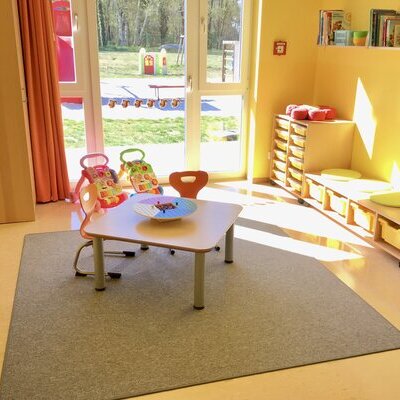 Schlaf und Spielraum der Zwerge. Mittig steht ein kleiner Tisch mit 3 kleinen Stühlen. Im rechten Bildbereich ist eine flache Bank mit 4 Einschubkästen. Links daneben befindet sich etwas höheres Regal.