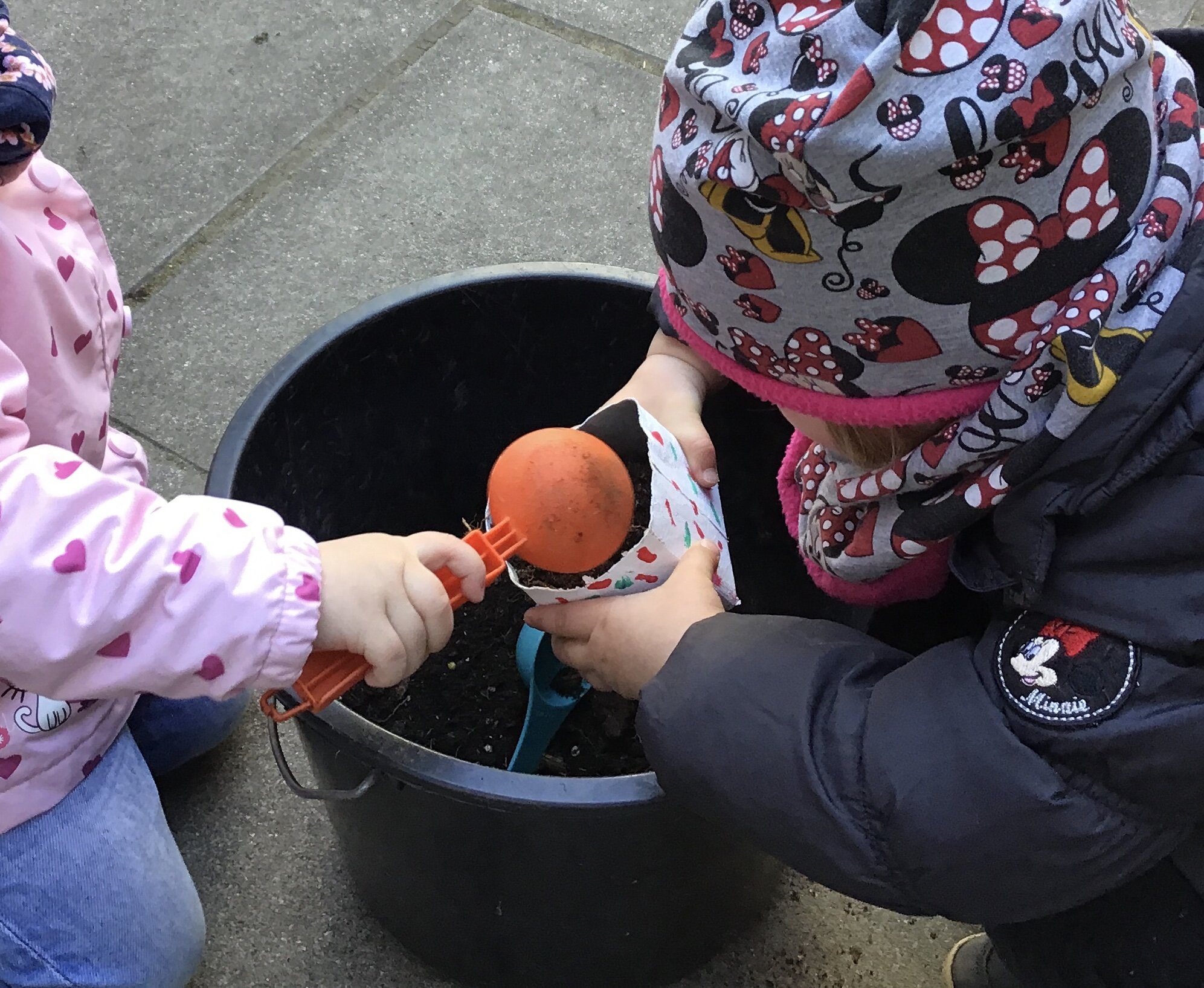 Zwei Kinder spielen über einem Eimer mit Sand.