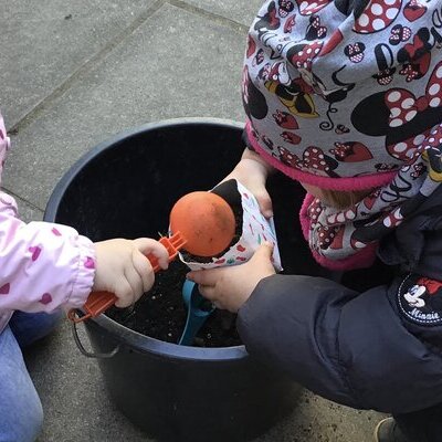 Zwei Kinder spielen über einem Eimer mit Sand.