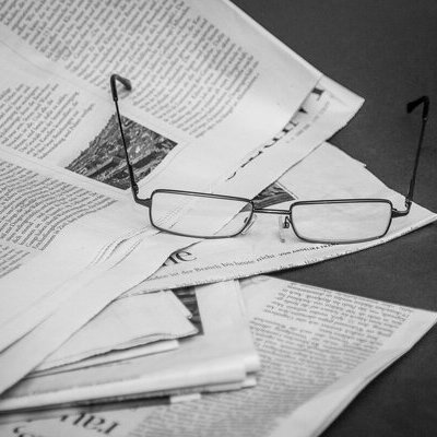 Mehrere aufeinander liegende Zeitungen und oben drauf liegt eine Lesebrille.