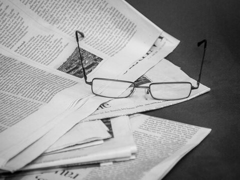 Mehrere aufeinander liegende Zeitungen und oben drauf liegt eine Lesebrille.